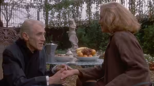 Don Corrado Prizzi (William Hickey) holds hands with a woman at an outdoor table
