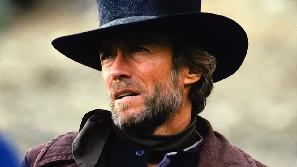 Preacher (Clint Eastwood) wearing a black hat and dark coat outdoors