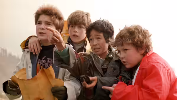 Four boys in jackets point ahead while holding a map