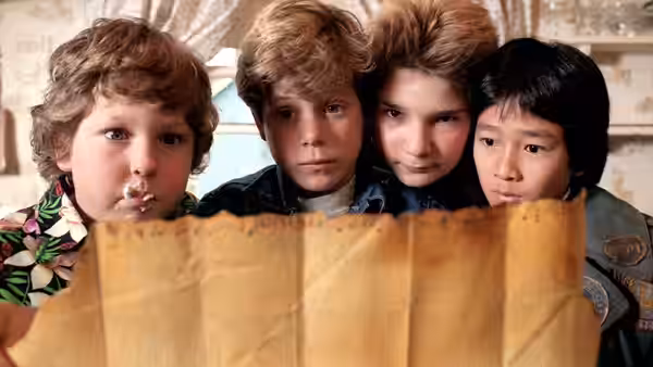 Chunk with ice cream peers at a map alongside three friends