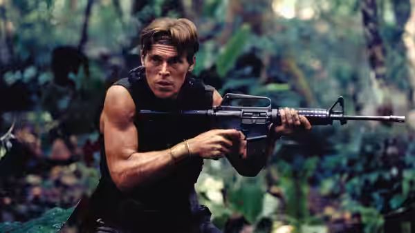 Soldier aims rifle while advancing through dense jungle foliage