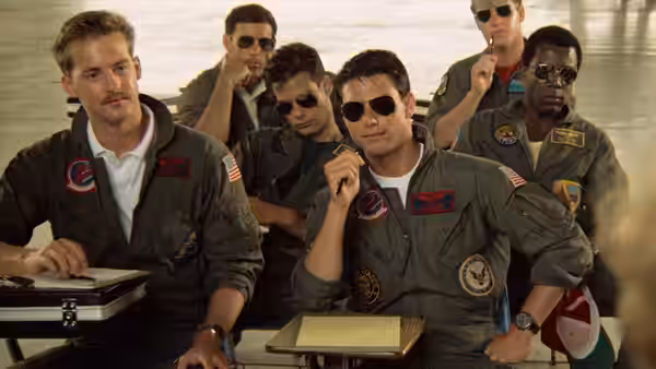 Maverick (Tom Cruise) sits with fellow pilots at a briefing table