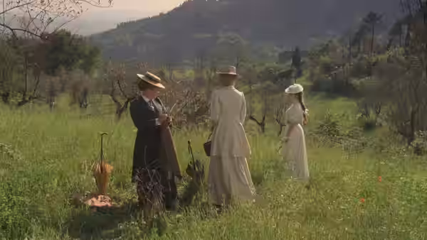 Three women standing together in a green field with hills behind them