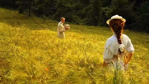 Man holding hat facing woman standing in a sunlit grassy field