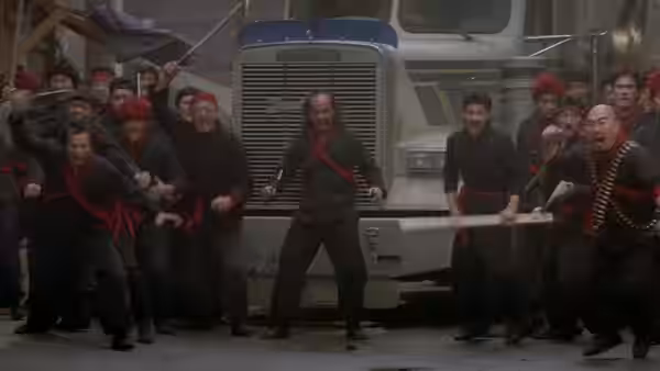 A crowd of men in black restrain a figure before a large truck