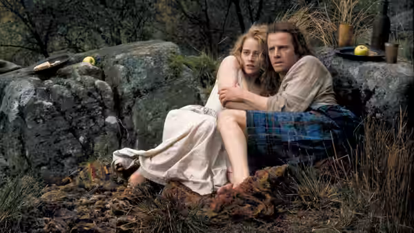 Connor MacLeod (Christopher Lambert) sits with Heather (Beatie Edney) on rocks in the woods