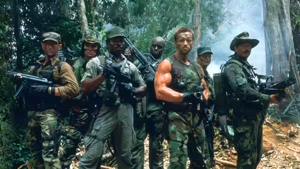Dutch (Arnold Schwarzenegger) standing with armed soldiers in the jungle