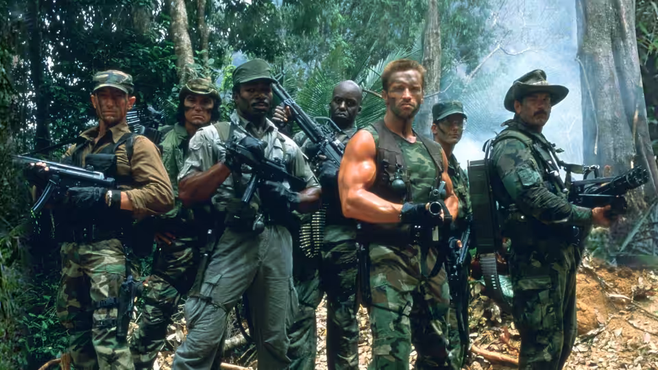 Dutch (Arnold Schwarzenegger) standing with armed soldiers in the jungle
