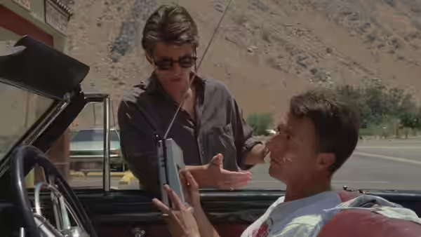 Tom Cruise in a convertible speaking with a man holding a radio