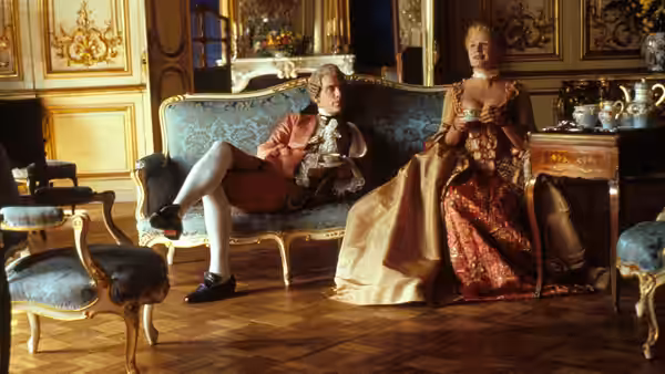 Vicomte de Valmont (John Malkovich) lounges on a sofa beside an older woman