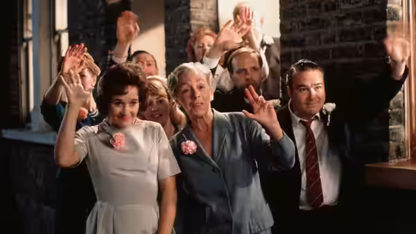 A group of people wave while standing outside a brick building