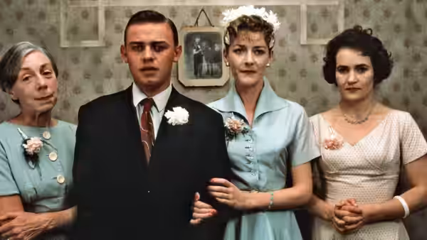 A groom in a suit poses with a bride and two other women