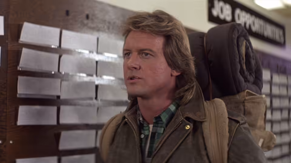 John Nada (Roddy Piper) standing before a job opportunities board