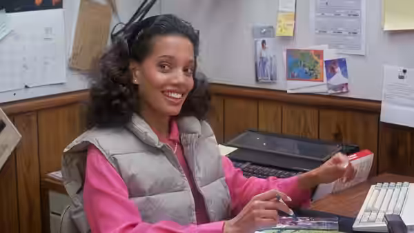 Lisa McDowell (Shari Headley) smiling at a desk in an office