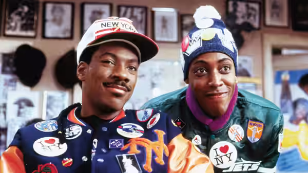 Eddie Murphy and Arsenio Hall in sports jackets and novelty hats indoors