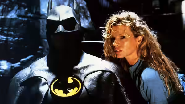 Batman (Michael Keaton) standing beside Vicki Vale (Kim Basinger) near rocks