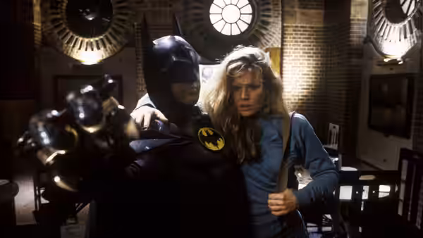 Batman (Michael Keaton) holding Vicki Vale (Kim Basinger) while aiming a weapon