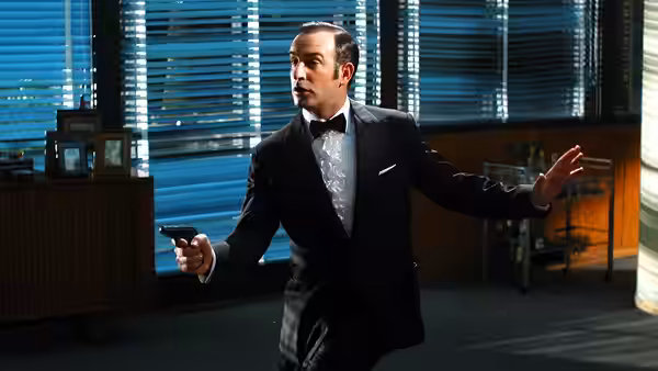 Hubert Bonisseur de La Bath (Jean Dujardin) holds a pistol and raises his free hand in an office