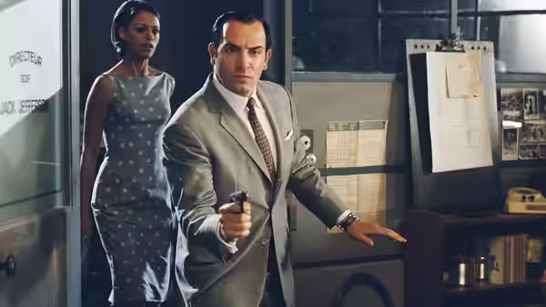 Hubert Bonisseur de La Bath (Jean Dujardin) enters an office with a pistol as Larmina follows