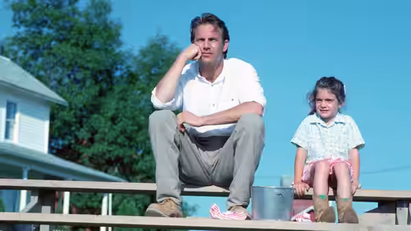 Ray Kinsella (Kevin Costner) sits on bleachers beside young Karin Kinsella (Gaby Hoffmann)