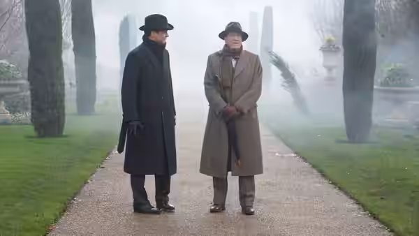 Two men in overcoats and hats standing on a misty garden path
