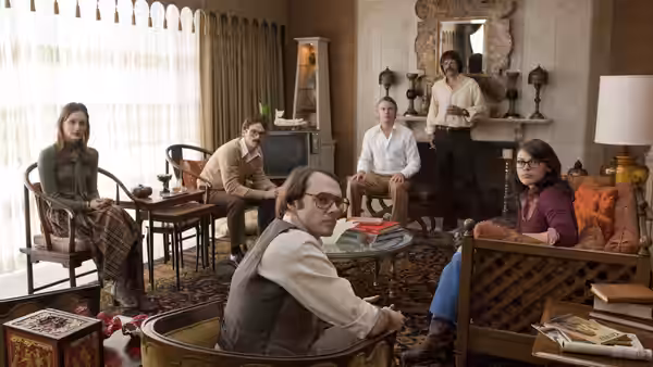 A group of men and women sit and stand together in a furnished living room