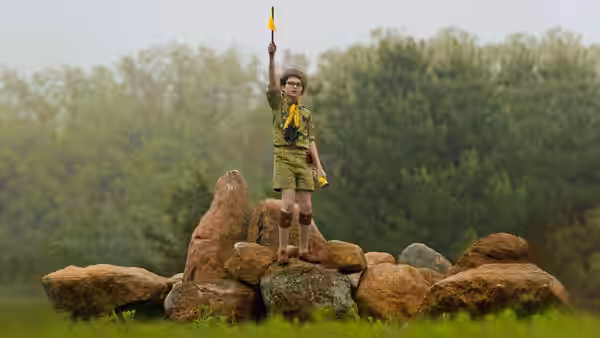 Sam Shakusky (Jared Gilman) holding a yellow flag on a pile of rocks