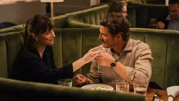 Lucy (Dakota Johnson) holding hands with Harry (Pedro Pascal) at a restaurant table