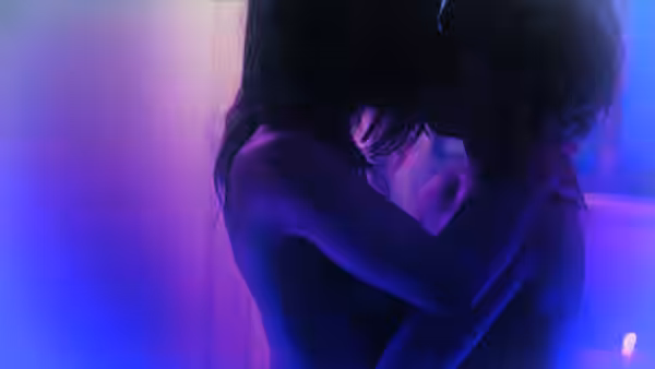 Two young women sharing a close embrace in dim blue lighting
