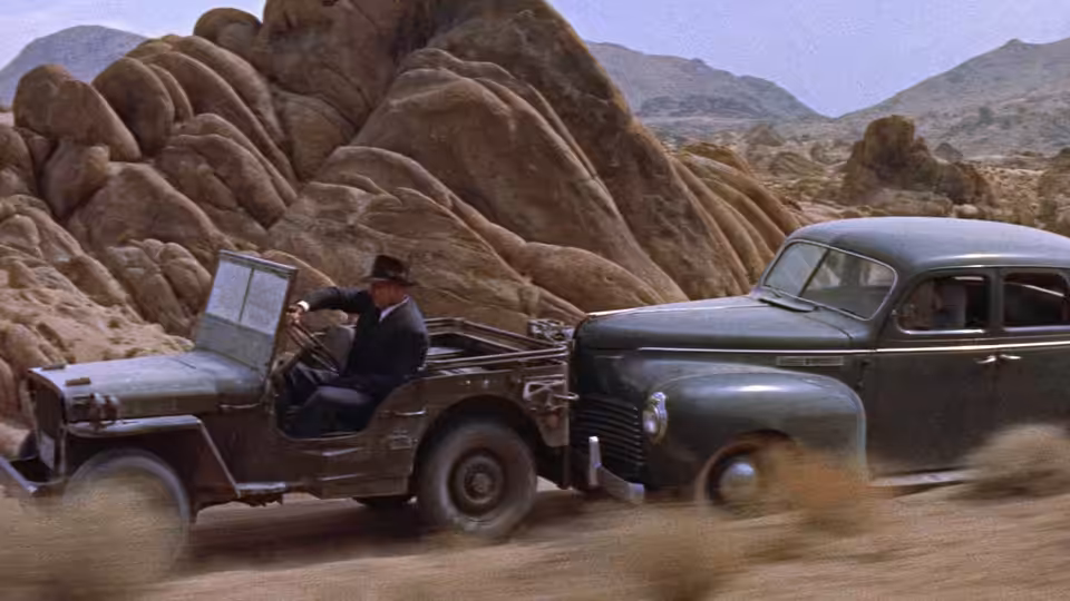 John J. Macreedy sits in a pickup truck beside towering rocks in the desert