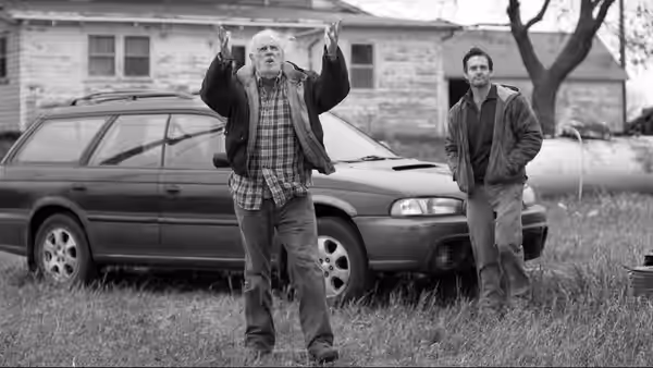 Woody Grant (Bruce Dern) raises both arms beside a station wagon while David Grant (Will Forte) watches