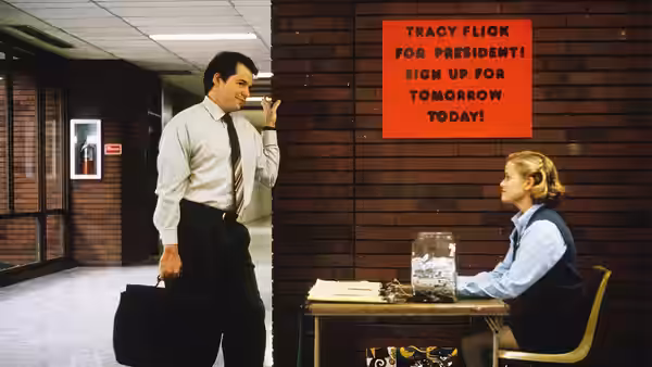 Jim McAllister (Matthew Broderick) reads a campaign poster near Tracy Flick at her table