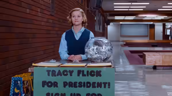 Tracy Flick (Reese Witherspoon) stands behind her sign-up table in a school hallway
