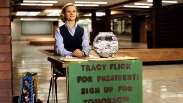 Tracy Flick (Reese Witherspoon) stands behind her campaign table in a school hallway