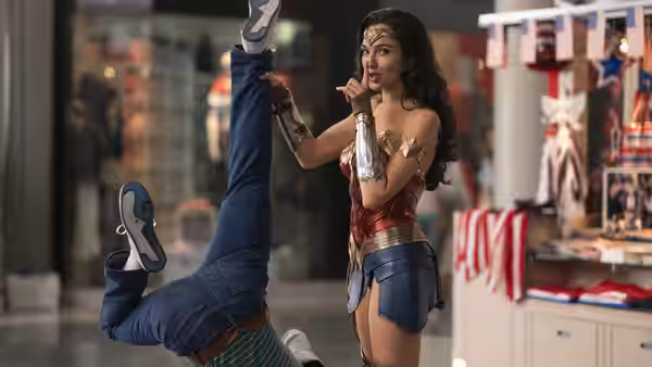 Diana Prince (Gal Gadot) stands in a shop as an attacker flips upside down beside her