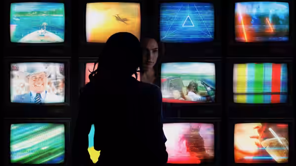 Diana Prince (Gal Gadot) watches a wall of televisions beside a silhouetted figure