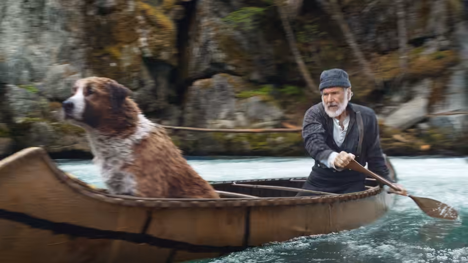 John Thornton (Harrison Ford) paddles a canoe downriver with Buck beside him