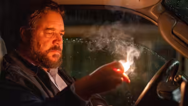 Tom Cooper (Russell Crowe) sits in a car, holding a smoking object