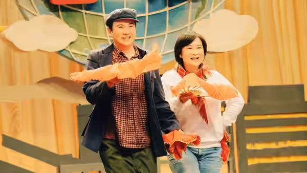 A man and woman perform with orange feathered props on a decorated stage
