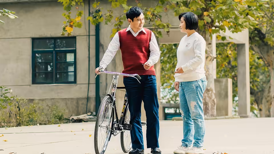 A man stands beside his bicycle talking with a woman outside a building