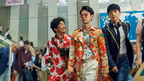 Tang Ren (Wang Baoqiang) and Qin Feng (Liu Haoran) walk beside a man in a floral suit through a busy concourse