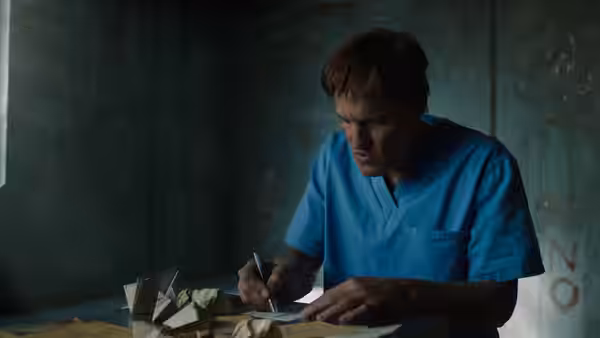 Dr. Dan Lewis (Reid Scott) writes at a table in blue scrubs