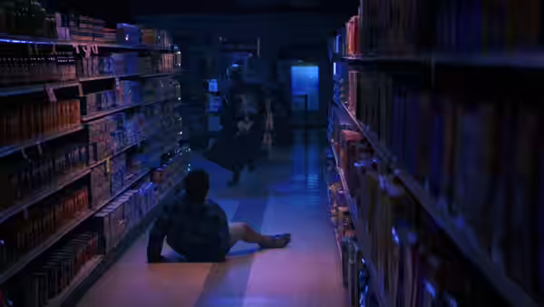 A skull-masked figure approaches someone fallen in a dimly lit store aisle