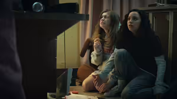 Samantha (Olivia Scott Welch) and Deena (Kiana Madeira) crouch beside a cabinet