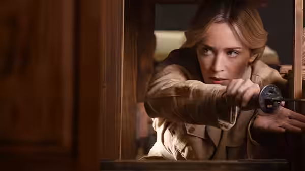 Dr. Lily Houghton (Emily Blunt) leans through a wooden hatch, aiming a pistol