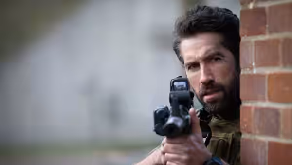 Jake Harris (Scott Adkins) aims his rifle around a brick corner