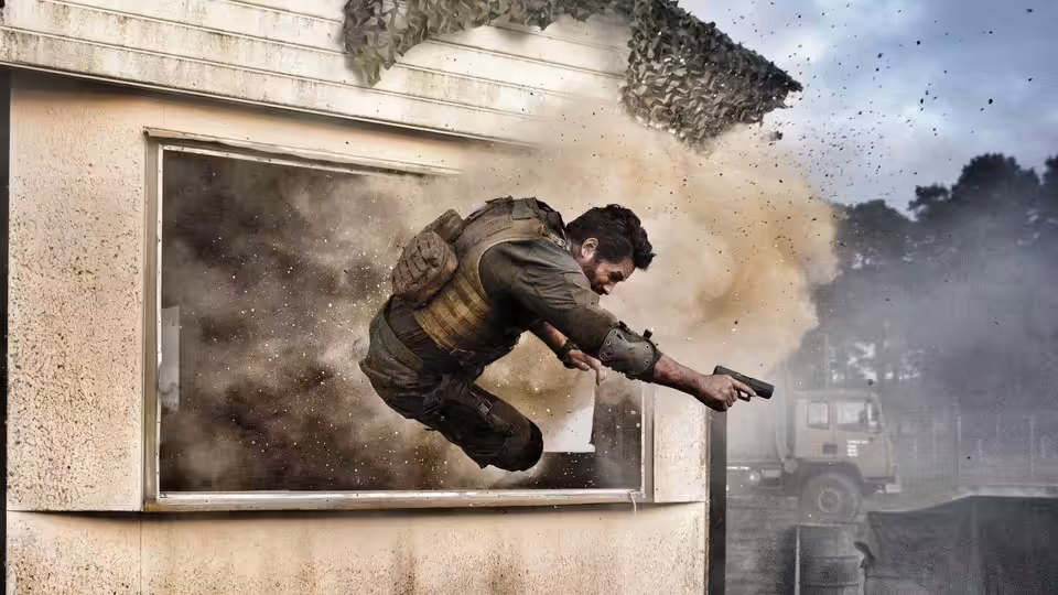 Jake Harris (Scott Adkins) dives through a window as an explosion blasts debris behind him