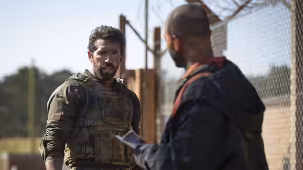 Jake Harris (Scott Adkins) speaks with a man beside a chain-link fence