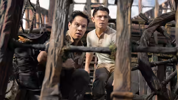 Nathan Drake (Tom Holland) and Sully (Mark Wahlberg) crouch behind wooden beams aboard a ship