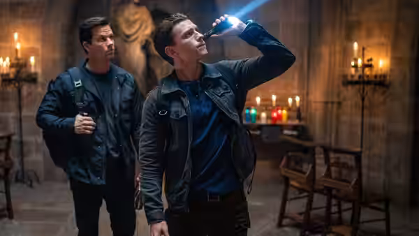 Nathan Drake (Tom Holland) examines a glowing object in a candlelit church as Sully (Mark Wahlberg) watches